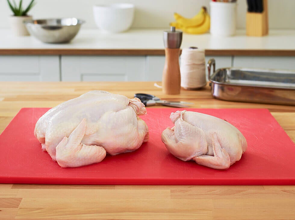 One small and one large whole raw chicken laid out on a red cutting board