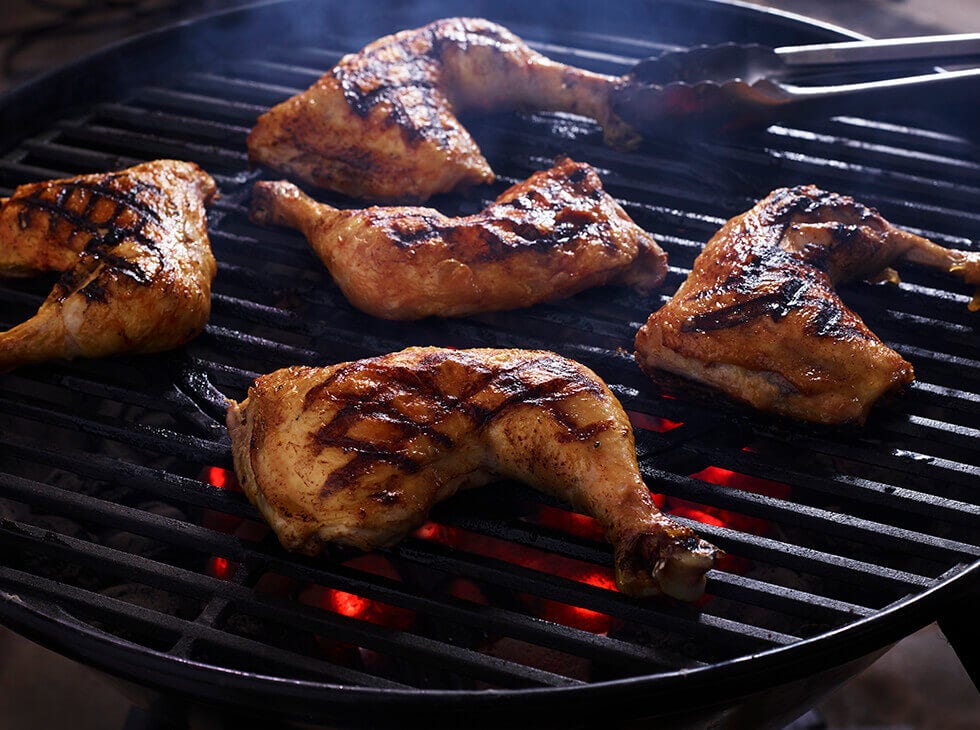 Chicken leg quarters grilling over an open flame on bbq grill featuring grill marks