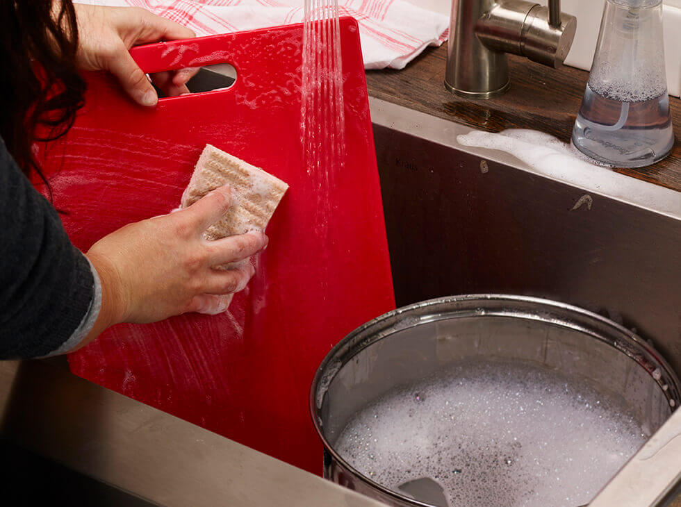 red cutting board being washed with a sponge
