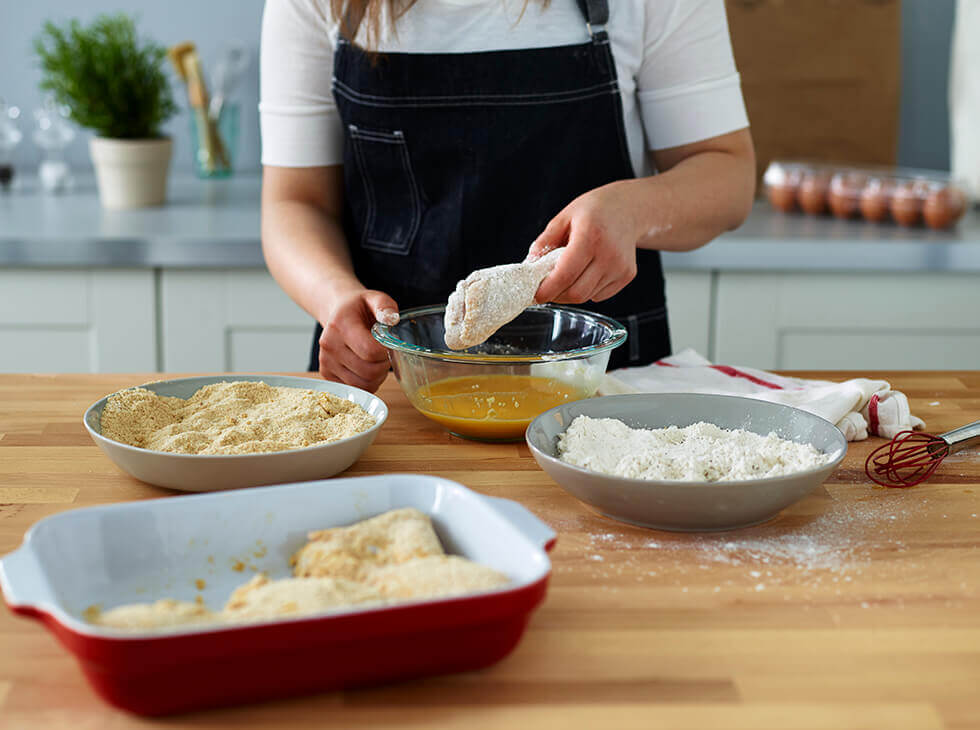 Chicken being breaded with bread crumbs, egg and flour