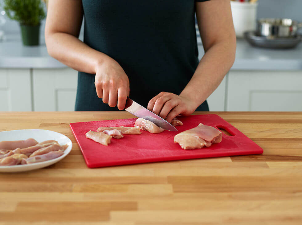 Chicken on a red cutting board being cut with a knife