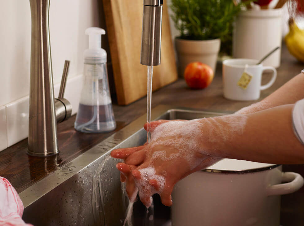 person washing their hands in the kitchen sink with soapy water