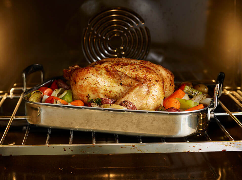 Whole chicken roasting in the oven with vegetables in a metal baking pan