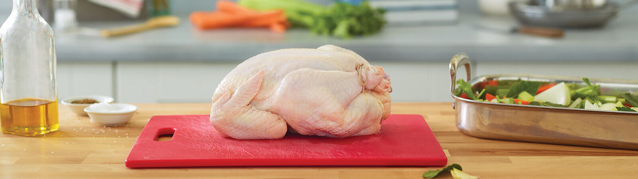 Whole raw chicken on a cutting board with a seasoning off the side